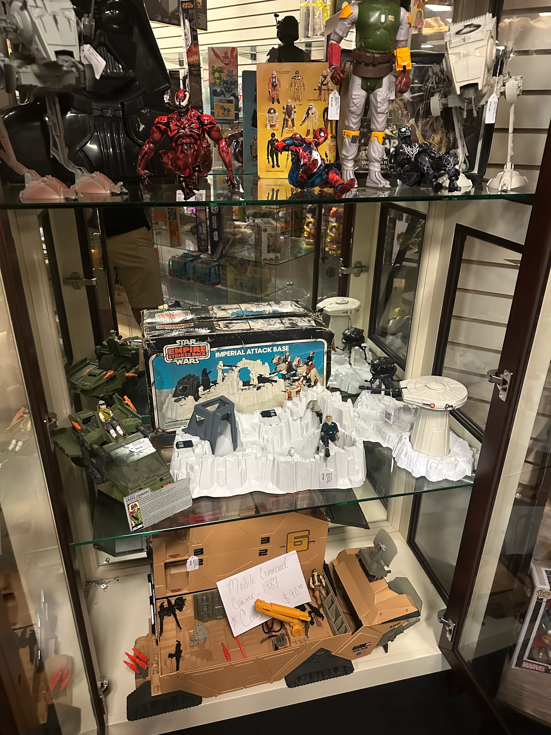 A glass cabinet filled with Star Wars, GI Joe, vehicles, and playsets